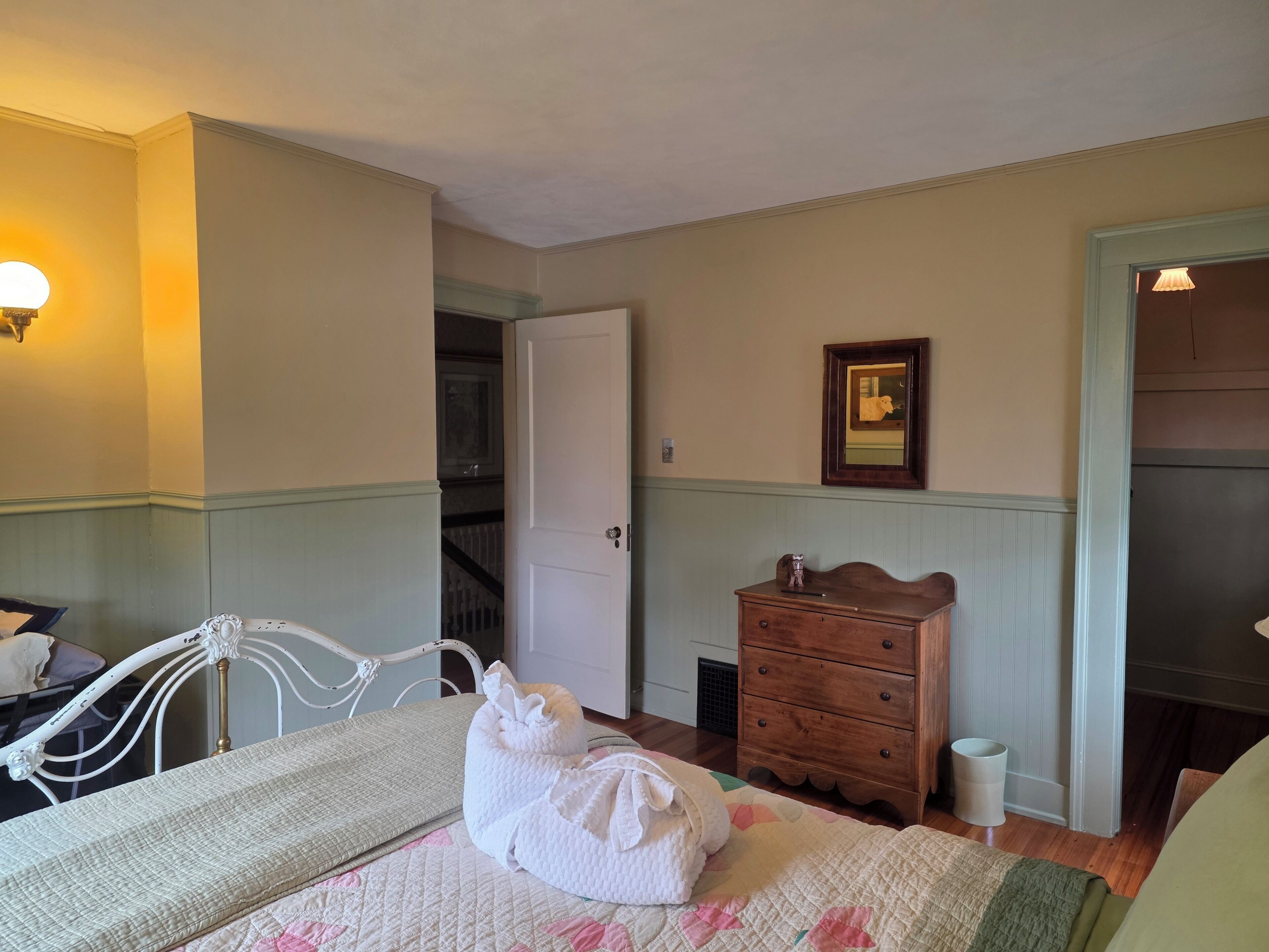 A hotel room with a bed, a dresser, a mirror, and a door leading to a staircase.