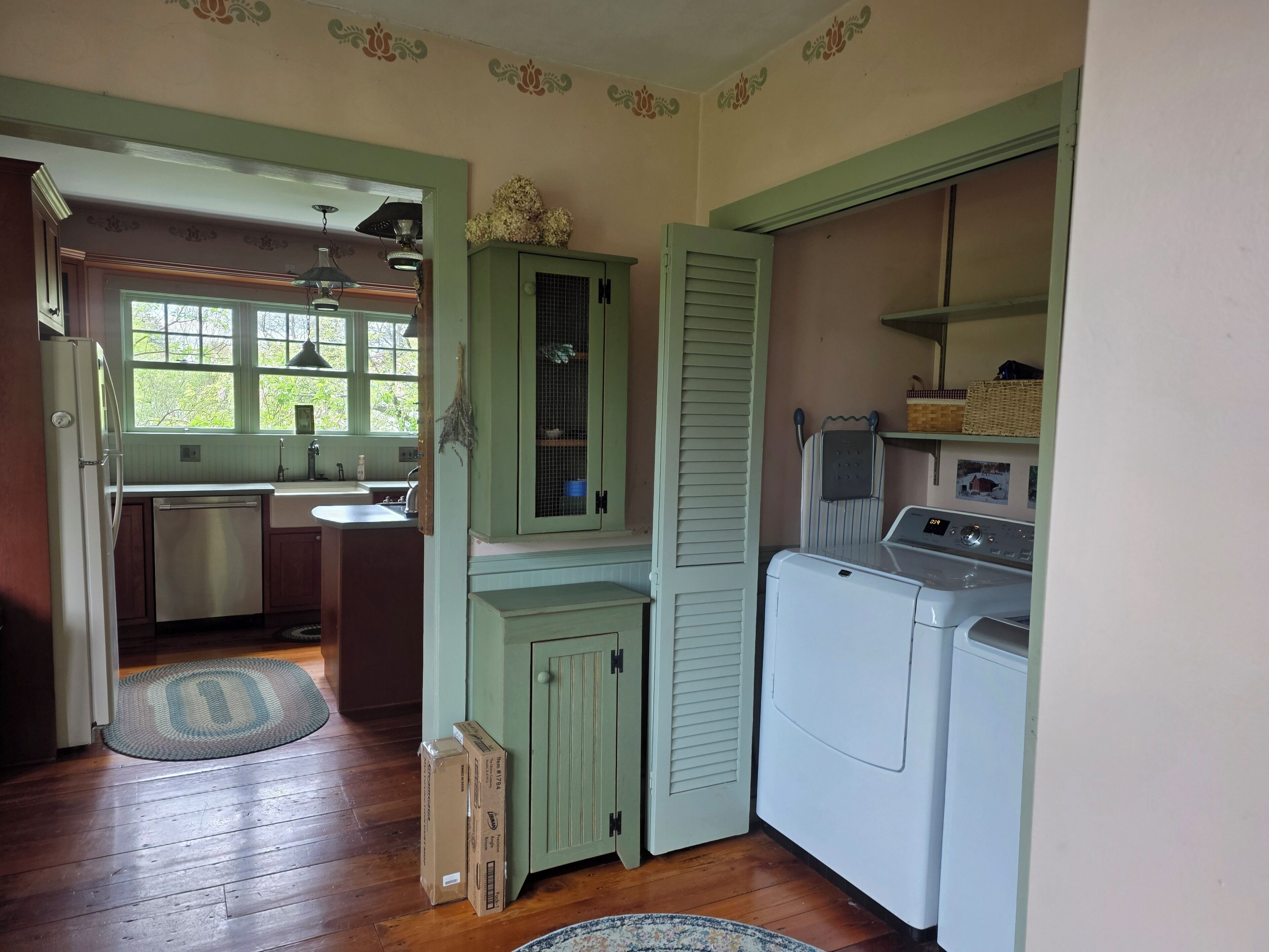 A compact kitchen with a built-in washer and dryer, a window with a view of greenery, and a door leading to another room.