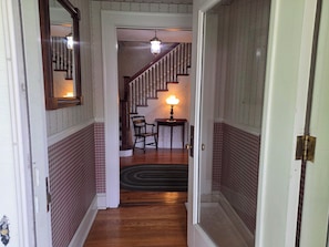 A hallway with a wooden floor, a chair, a lamp, and a staircase with a railing.