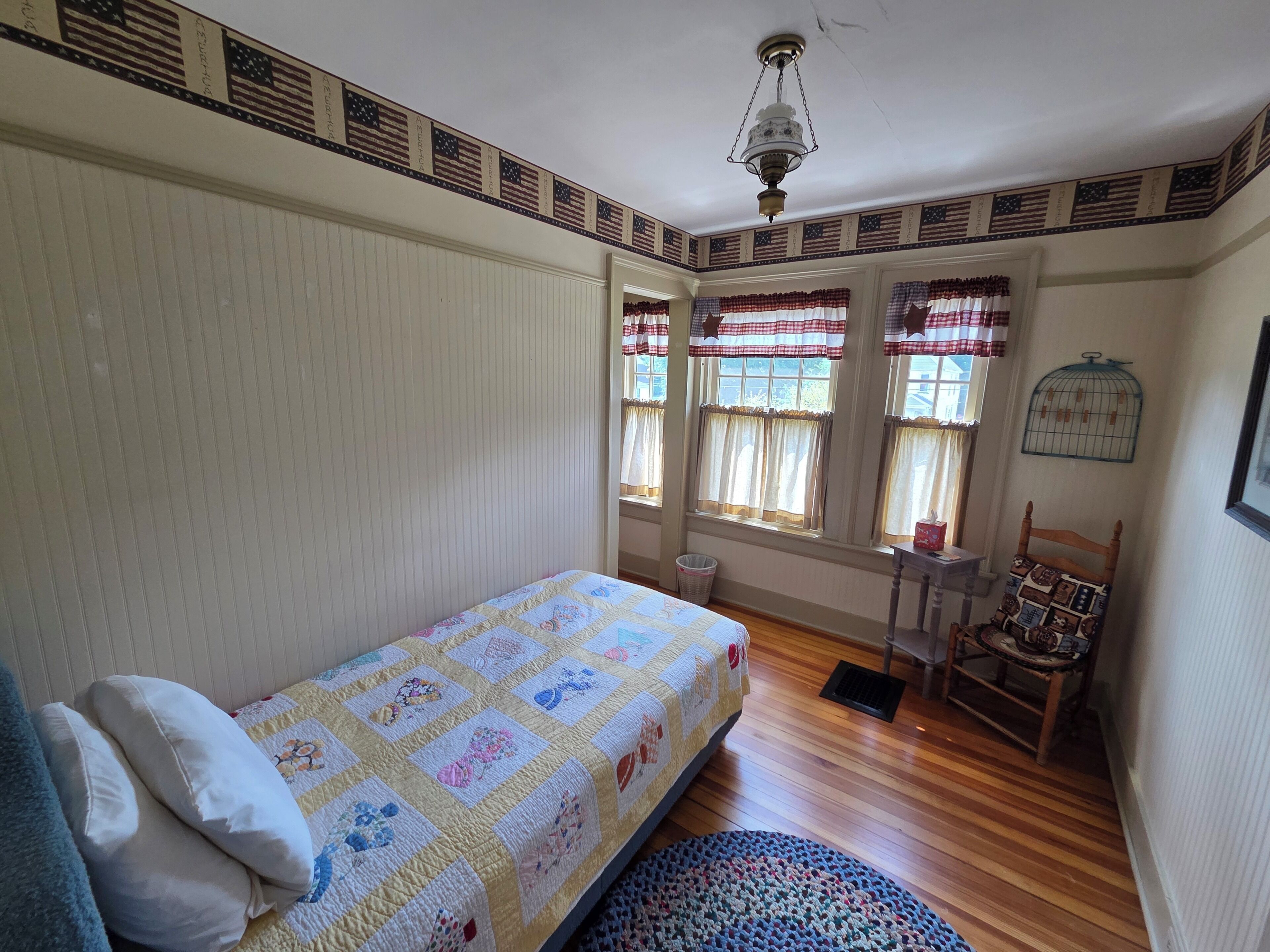 Una habitación con cama, una silla, una mesita y una ventana con cortinas.