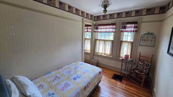 Una habitación con cama, una silla, una mesita y una ventana con cortinas.
