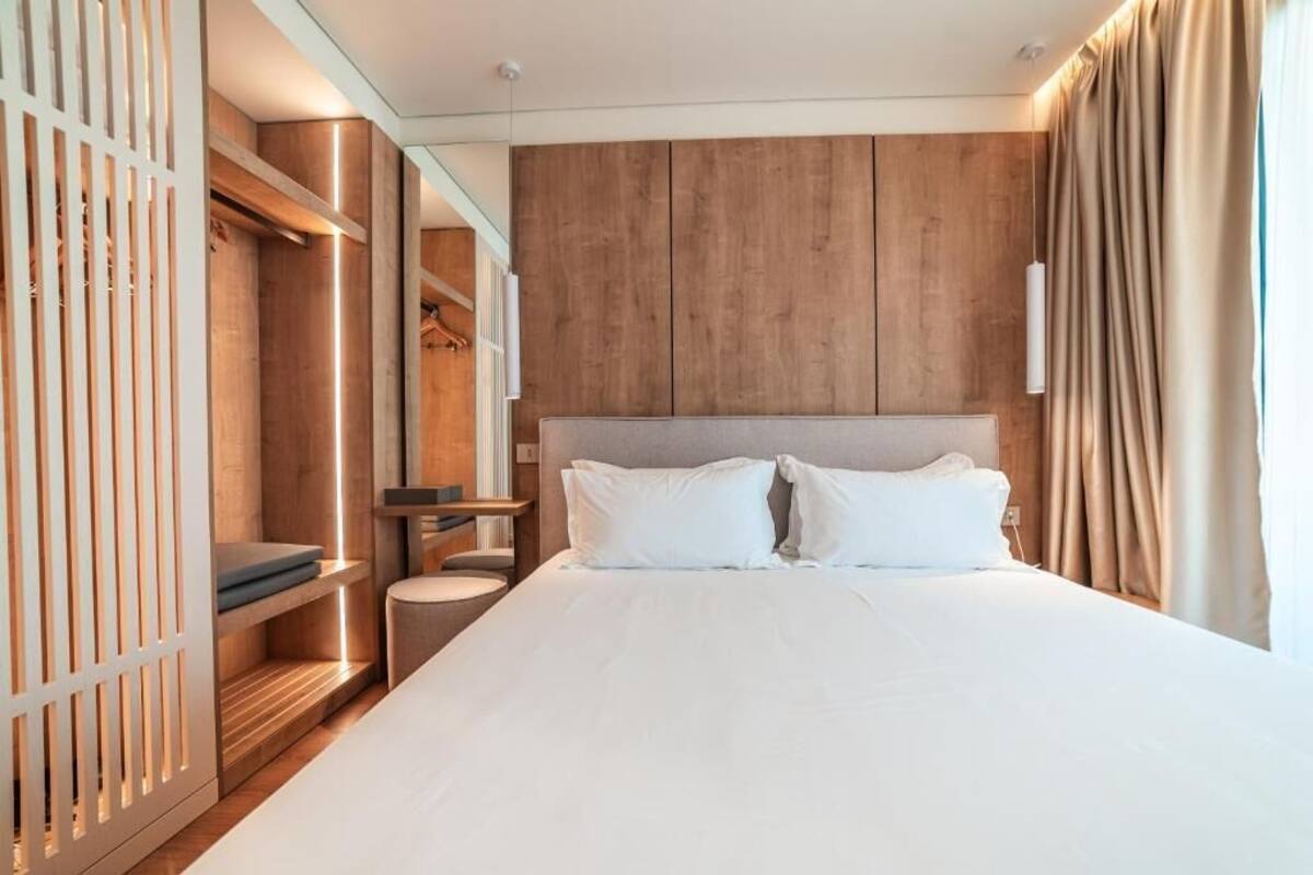 Una habitación de hotel moderna con una cama grande, paneles de madera, un armario empotrado y una mesita de noche.