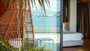 Una habitación de hotel moderna con pared de vidrio, una cama, una mesita pequeña y una silla de mimbre.