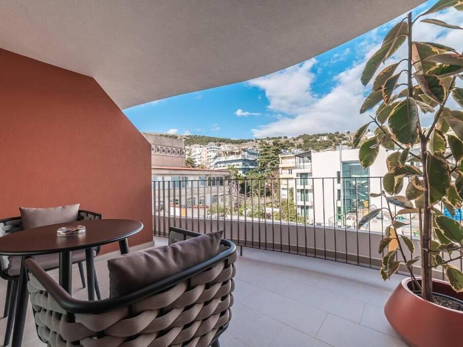 A balcony with a table and chairs, a potted plant, and a view of buildings and hills.