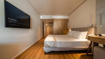 A modern hotel room with a bed, a desk, a television, and a wardrobe.