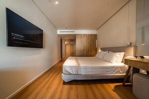 A modern hotel room with a bed, a desk, a television, and a wardrobe.