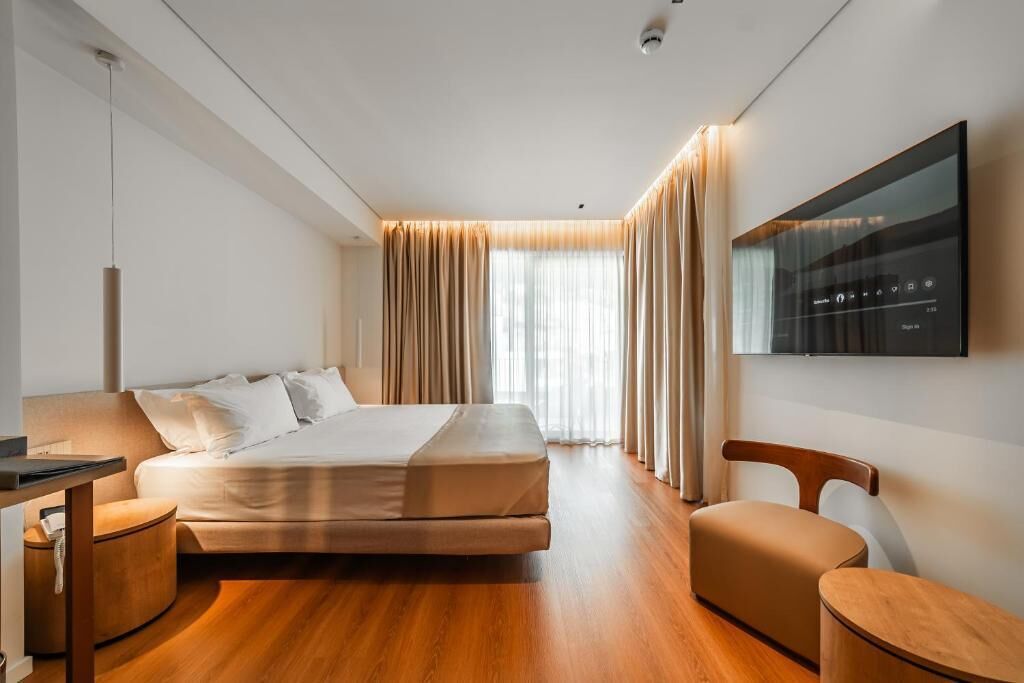 Ein modernes Hotelzimmer mit einem Bett, einem Schreibtisch, einem Sessel und einem an der Wand montierten Fernseher.
