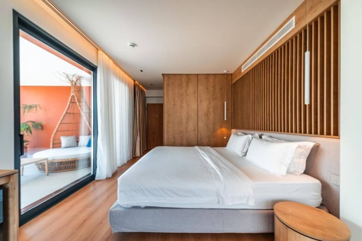 Un dormitorio moderno con una cama grande, paneles de madera, una mesita de noche y vistas a un balcón exterior.
