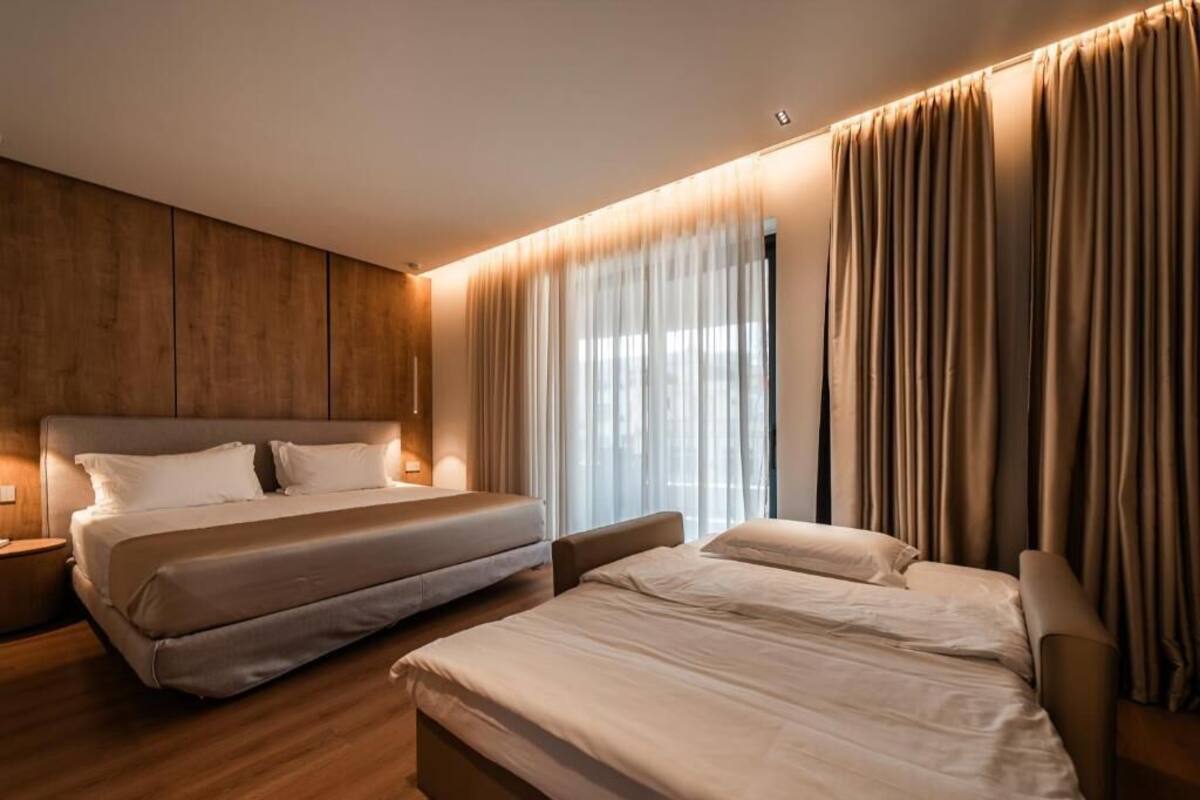 Habitación de hotel con una cama grande, una cama más pequeña, un escritorio y una ventana con cortinas.