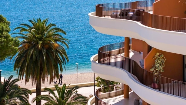 Un edificio de varios pisos con balcones que dan a una playa y al mar.