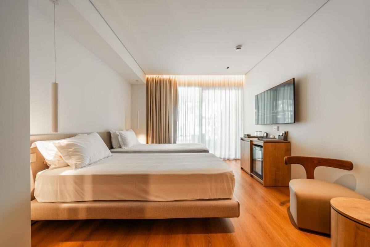 Habitación de hotel con dos camas, un escritorio, una silla y un televisor en la pared.