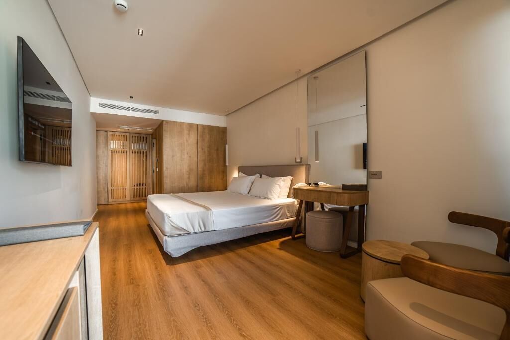 A modern hotel room with a wooden floor, a bed, a desk, a chair, and a mirror.