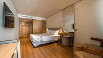 A modern hotel room with a wooden floor, a bed, a desk, a chair, and a mirror.