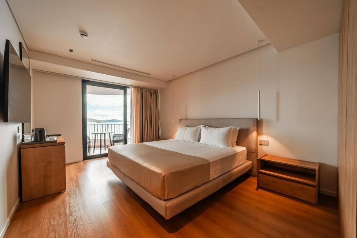 Habitación de hotel moderna con una cama grande, un escritorio pequeño, un televisor y un balcón con vistas.