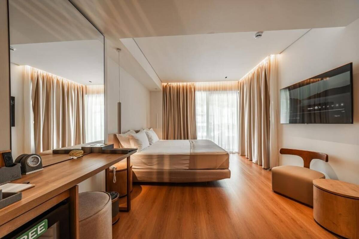 Habitación de hotel moderna con cama, escritorio, silla, televisor y un espejo grande.