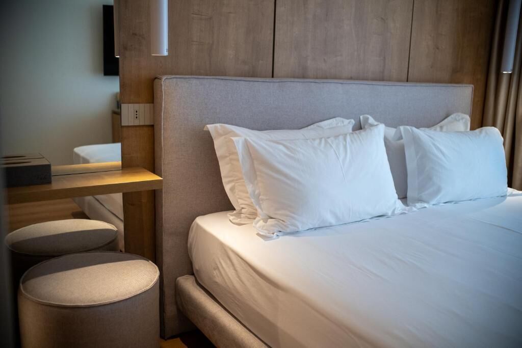 Hotellihuone, jossa on sänky, yöpöytä ja seinälle asennettu televisio.
