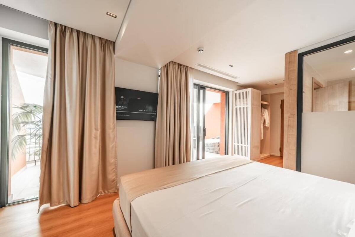 Habitación de hotel con cama, televisor, puerta corredera y ventana grande.