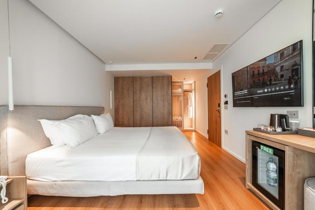 A modern hotel room with a large bed, a TV mounted on the wall, and a small cabinet with a water dispenser.