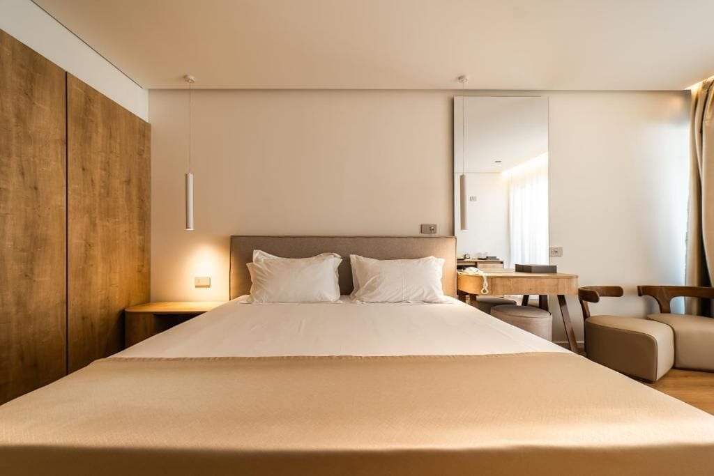 A modern hotel room with a large bed, a wooden accent wall, a desk with a chair, and a large mirror.