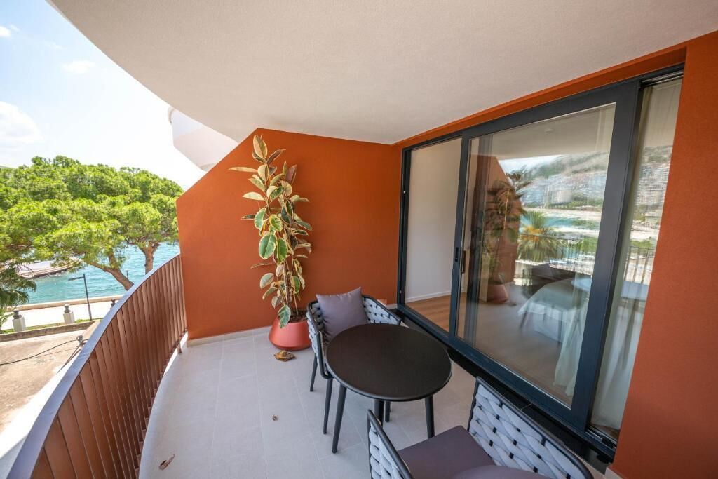 Un balcón con una mesa y sillas, una planta en maceta y vistas a una piscina y vegetación.
