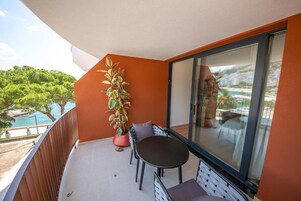 Un balcón con una mesa y sillas, una planta en maceta y vistas a una piscina y vegetación.