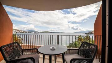 Ein Balkon mit zwei Korbstühlen und einem kleinen runden Tisch, mit Blick auf ein Gewässer und ferne Berge.
