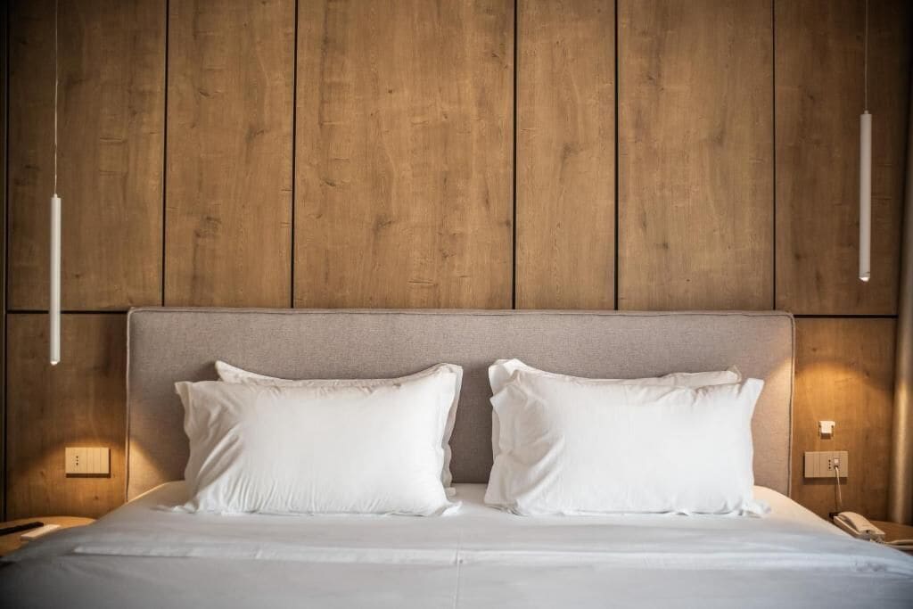 A bed with white linens, a neutral-toned headboard, and a wooden wall paneling.