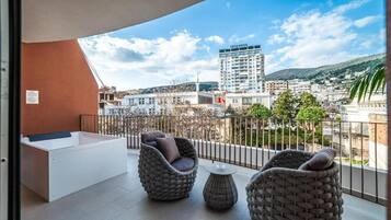A balcony with a white bathtub, wicker furniture, and a view of a hotel and cityscape.