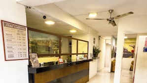 Un espace d’accueil d’hôtel comprenant un comptoir, un panneau affichant le menu et un ventilateur de plafond.