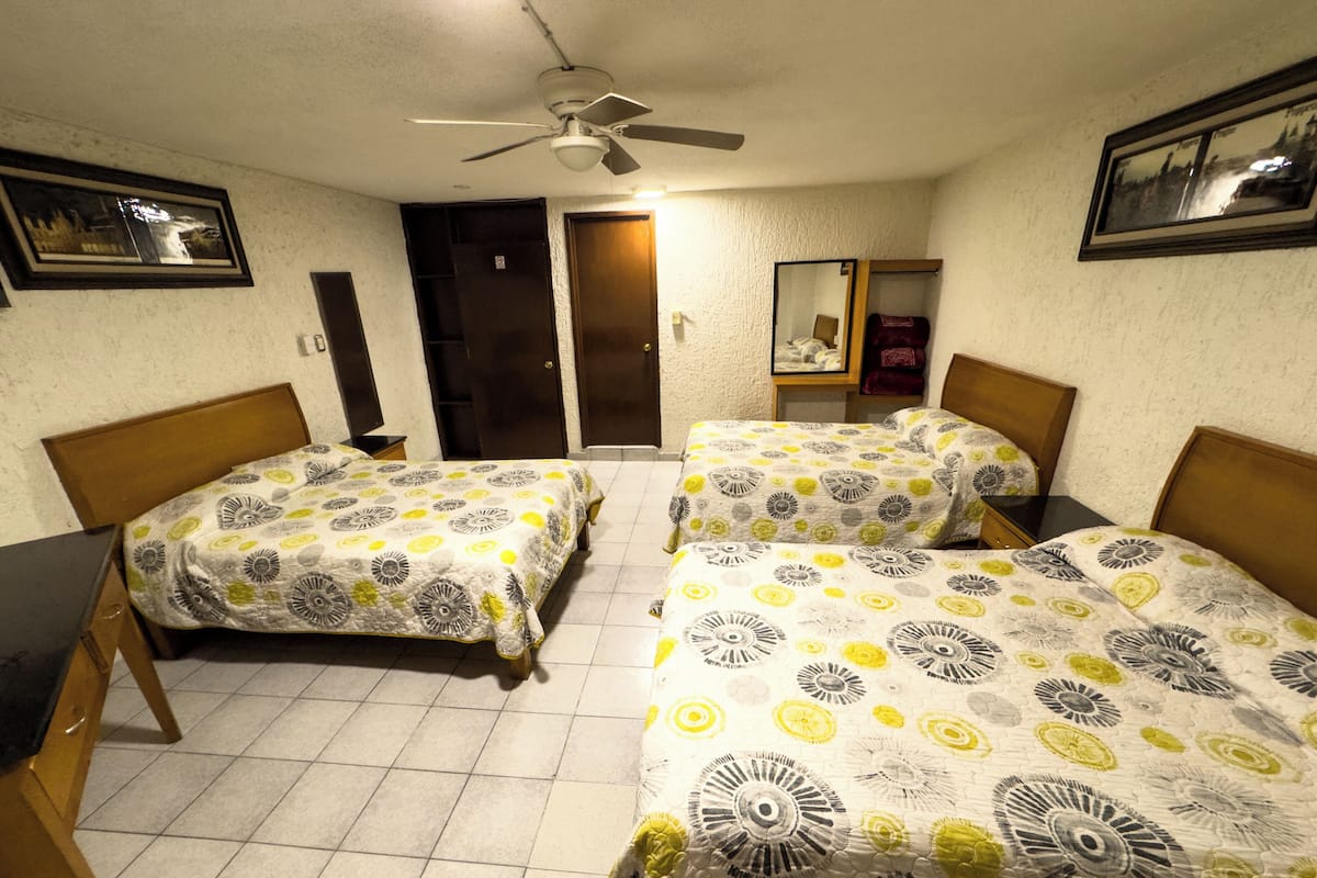 A room with two beds, a ceiling fan, a door, and a mirror on the wall.