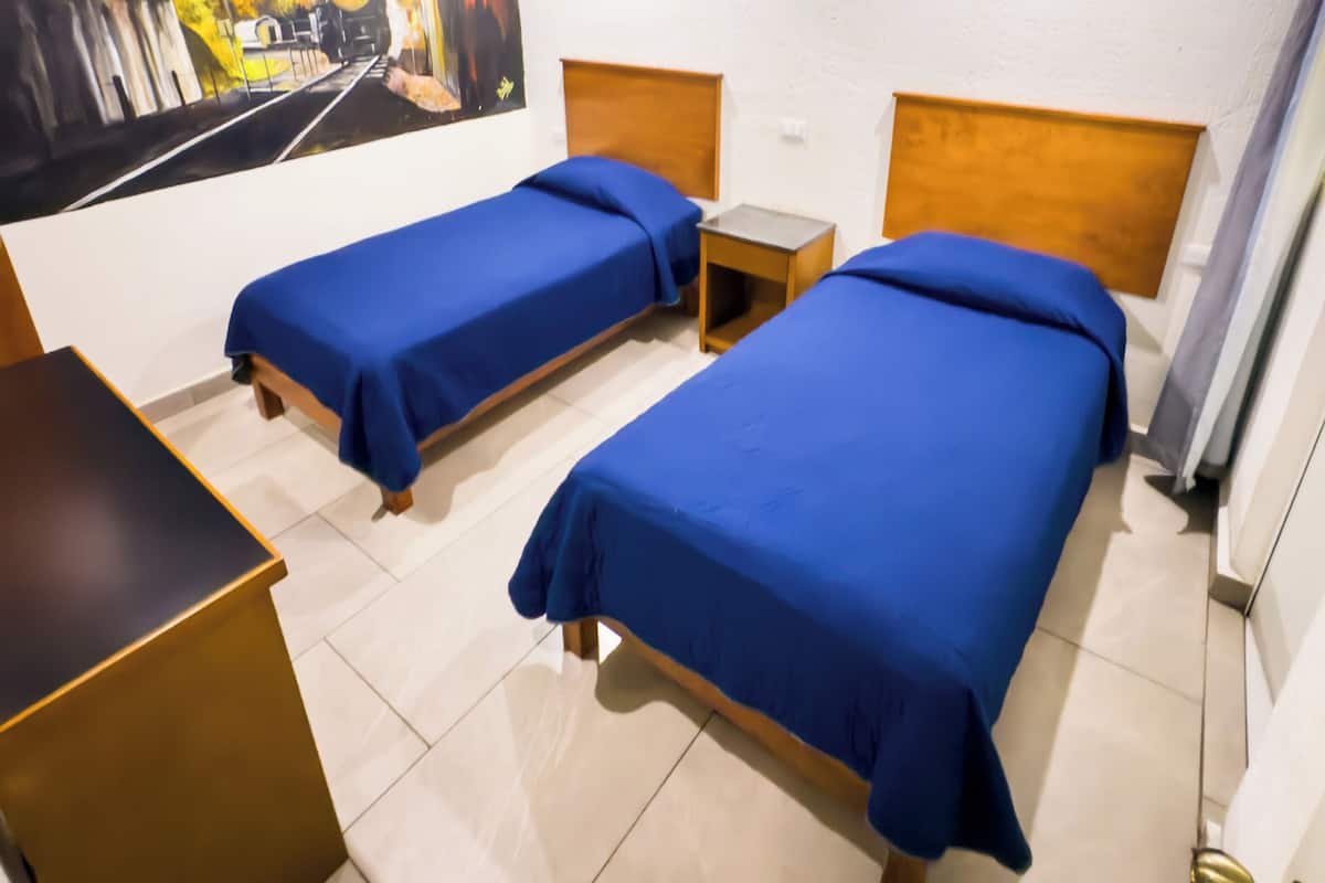 A hotel room with two single beds, a ceiling fan, a painting of a train tunnel, and a small table.
