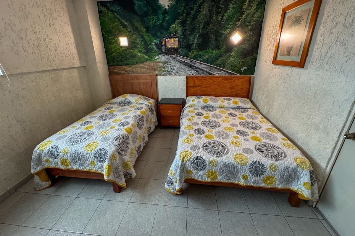 A small room with two single beds, a wooden headboard, a small nightstand, and a large forest-themed mural on the wall.