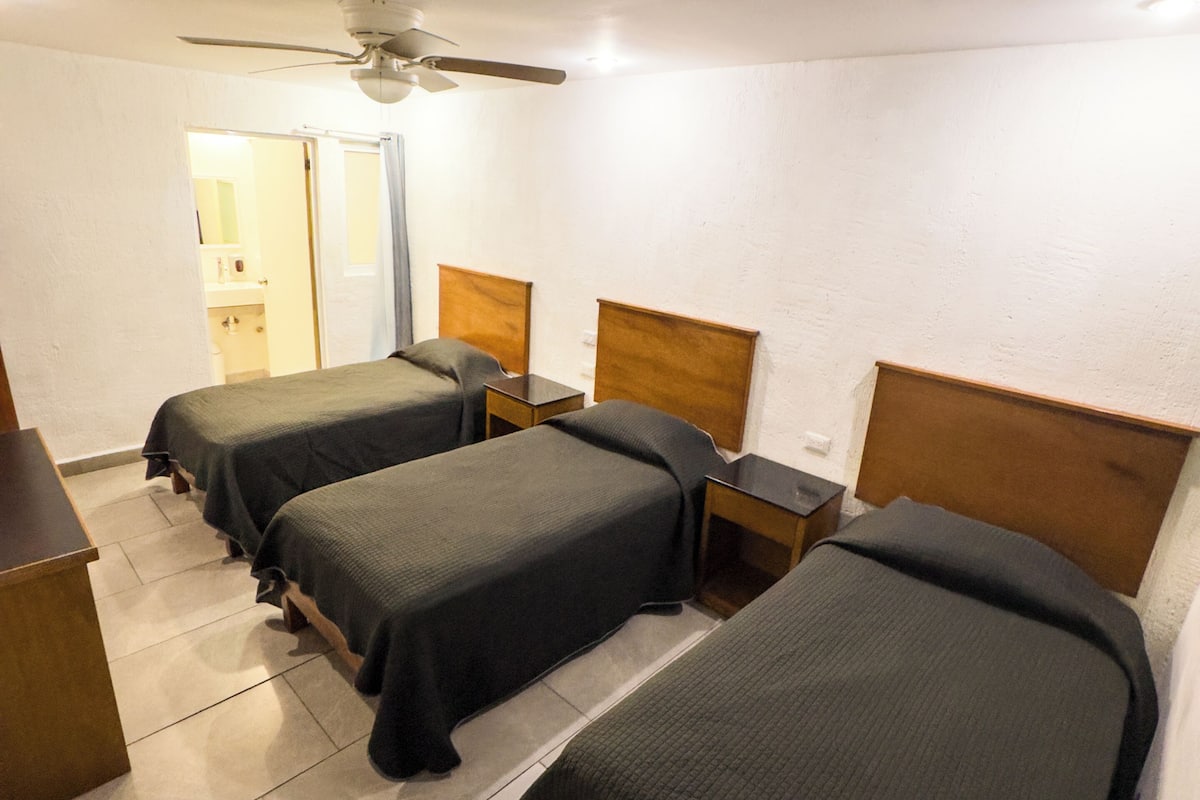 A hotel room with three single beds, a ceiling fan, and a bathroom visible through an open door.