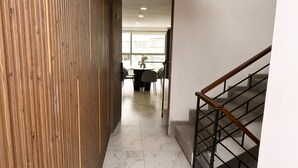 A hallway with a wooden wall, a staircase with a metal handrail, and a dining area with chairs and a table. - Luxury Penthouse in Polanco | Private Terraces + Prime Location (Ciudad de México)