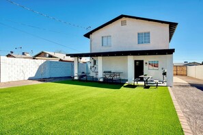 A two-story house with a covered patio, a well-maintained lawn, and a brick wall.