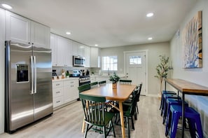 A modern kitchen with white cabinets, a stainless steel refrigerator, a microwave, and a dining area with green chairs and a wooden table.