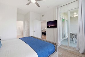 Une chambre avec un lit, une télévision, un ventilateur de plafond et une porte-fenêtre coulissante donnant sur un balcon.