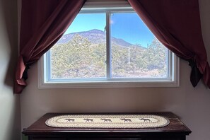 A window with curtains, a view of trees and mountains, and a mat with animal designs on a table. - Mountain Soul | ATV Access, Porch & Mountain Views (South Fork)