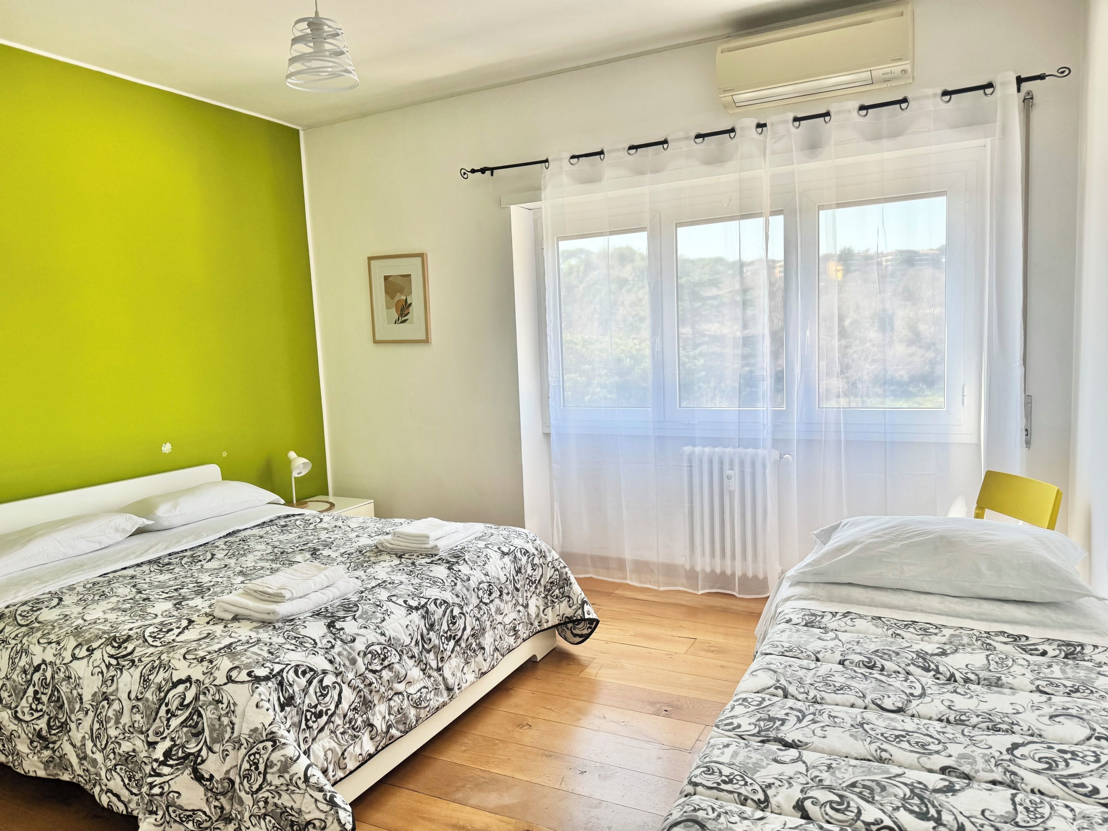 Un dormitorio con dos camas, una pared verde, una ventana con cortinas y un radiador.