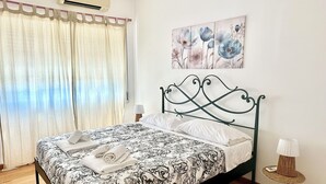 Une chambre à coucher avec un lit, des rideaux, un climatiseur, une lampe fixée au mur et un tableau.
