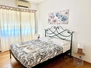 Ein Schlafzimmer mit einem Bett, Vorhängen, einer Klimaanlage, einer Wandleuchte und einem Gemälde.