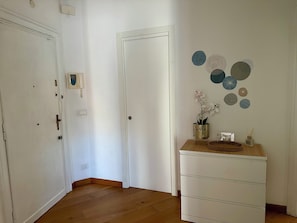 A hallway with wooden flooring, white walls, a white door, and a white dresser with decorative plates. - Vatican St. Peter bright apartment (Roma)