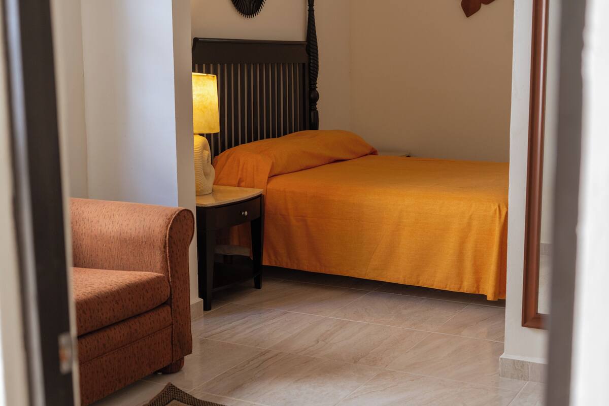A hotel room with a bed, a nightstand with a lamp, a chair, and a headboard.