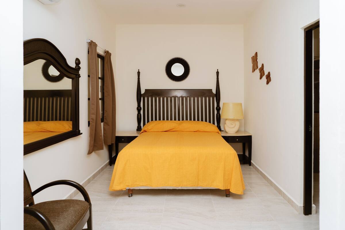A bedroom with a bed, a nightstand, a lamp, a mirror, and a chair.
