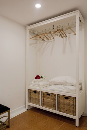 A white wardrobe with wooden hangers, a bed with white linens, and wicker baskets. - Graça Village Escape – 2BR Apartment (Lisbon)