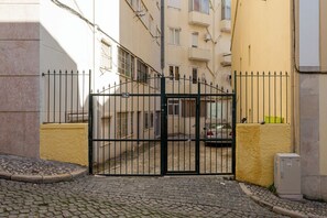 A gated entrance to a building with a cobblestone path, a yellow wall, and a utility box. - Graça Secret Village – 2BR Retreat (Lisbon)