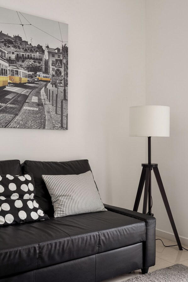 A black leather sofa with two pillows, a floor lamp, and a black and white photograph on the wall. - Graça Secret Village – 2BR Retreat (Lisbon)