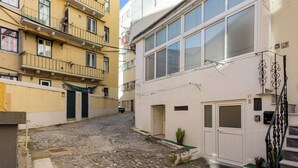 A narrow cobblestone street between buildings with balconies and a white door. - Graça Secret Village – 2BR Retreat (Lisbon)