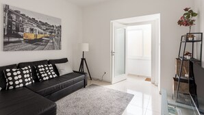 A modern living room with a black leather sofa, a large black and white painting, a glass door leading outside, and a small plant on a black shelf. - Graça Secret Village – 2BR Retreat (Lisbon)