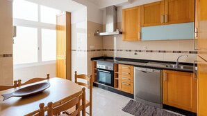 A kitchen with wooden cabinets, a stainless steel oven, a dishwasher, and a window providing natural light. - Graça Secret Village – 2BR Retreat (Lisbon)